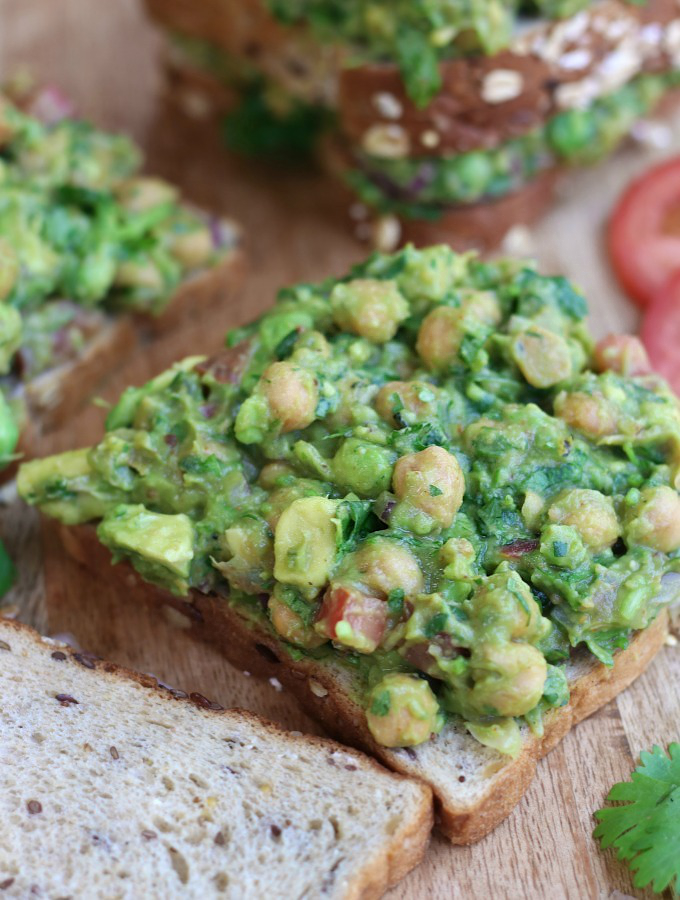 An open faced Guacamole Chickpea Salad Sandwich on a wooden cutting board.