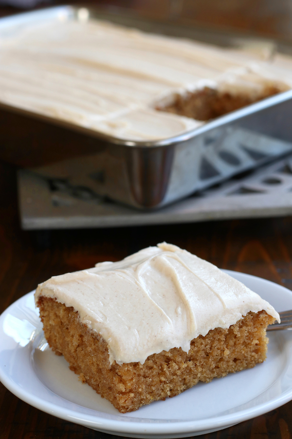 A piece of Apple Sauce Cake on a white plate sitting in front of the cut cake.