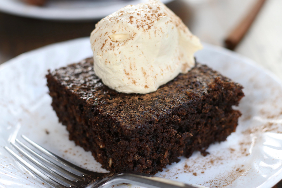 An up close photo of Molasses Cake served on a plate with whipped cream and cinnamon.