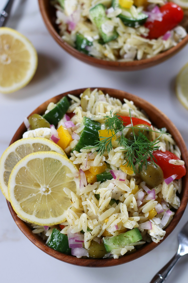 Orzo Salad served in two wooden bowls on a white surface.