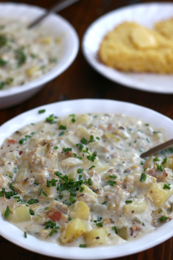 Two bowls of Best Clam Chowder Recipe sitting next to a plate of cornbread.