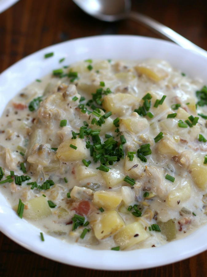 New England Clam Chowder in a white bowl sitting next to a soup spoon.