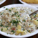 Thick New England Clam Chowder Recipe in white bowl sitting on a wooden table.