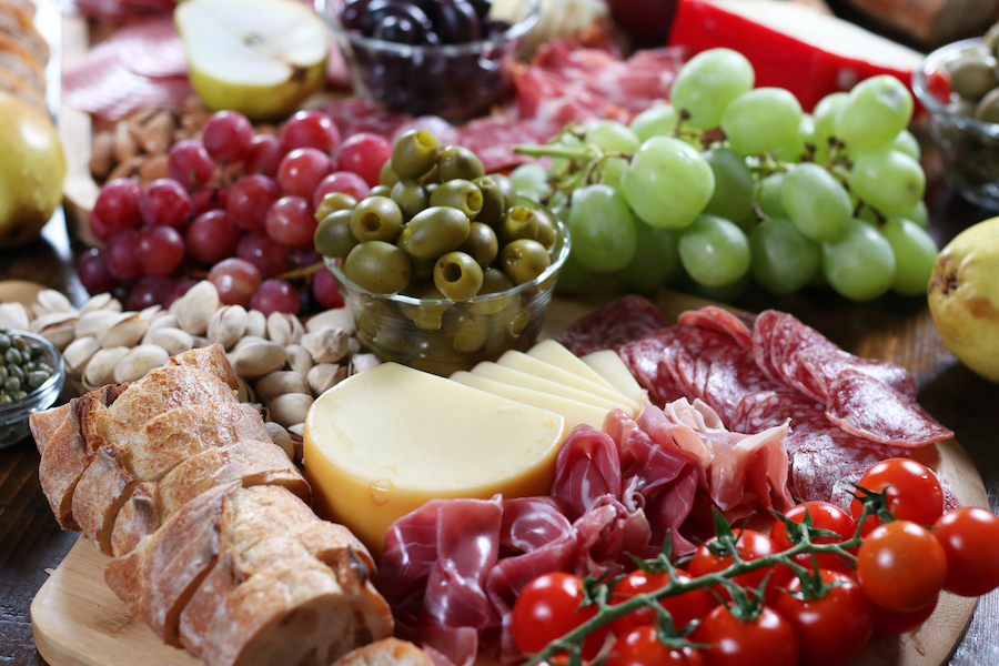 DIY Charcuterie Board with green grapes, red grapes, olives, meats, breads and cheese.