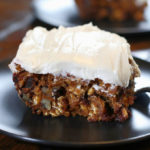 A slice of frosted Healthy Pumpkin Cake sitting on a black plate.