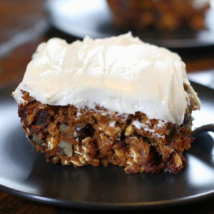 A slice of frosted Healthy Pumpkin Cake sitting on a black plate.