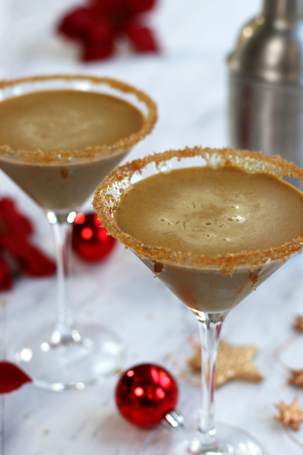 Two poured Christmas Cocktails in martini glass with Christmas ornaments sitting around the glasses.