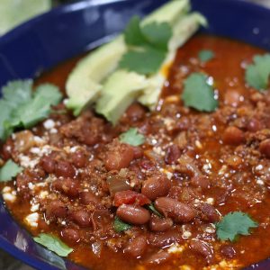 A bowl of Chorizo Beans garnished with cilantro, Mexican cheese crumbles and avocado slices.
