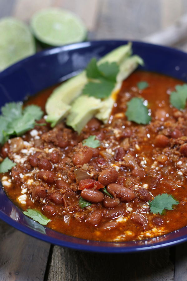 A bowl of Chorizo Beans garnished with cilantro, Mexican cheese crumbles and avocado slices.