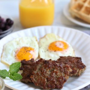 A table-scape of breakfast with Breakfast Sausage, eggs, waffles, blueberries and orange juice.