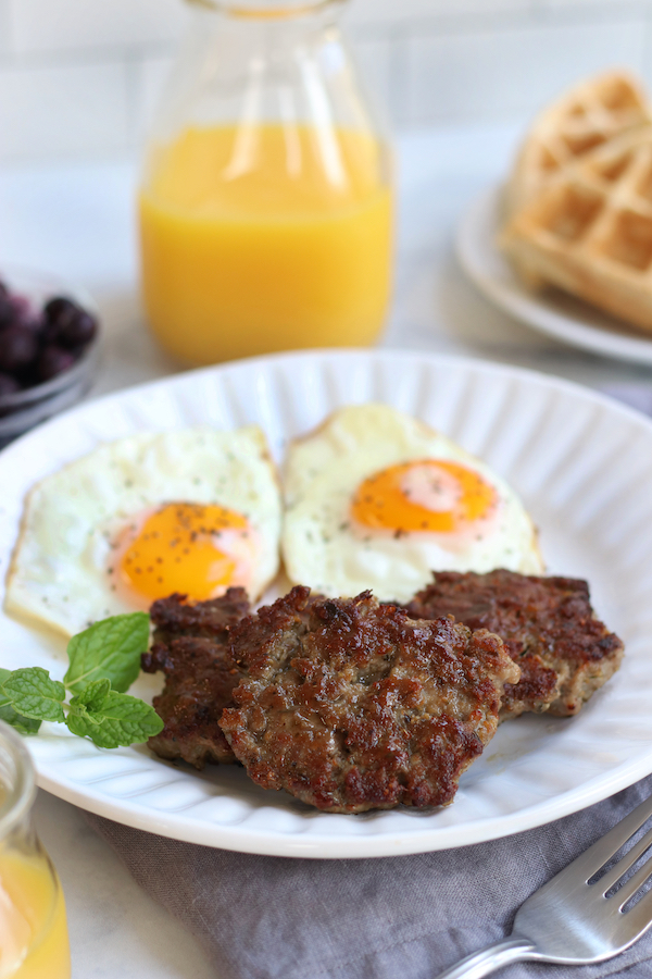 A table-scape of breakfast with Breakfast Sausage, eggs, waffles, blueberries and orange juice.