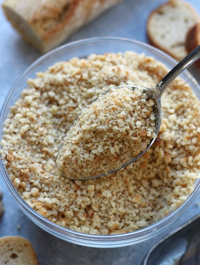 A spoon full of Homemade Breadcrumbs over a bowl of breadcrumbs.