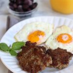 Three Homemade Breakfast Sausages on a white plate with sunny side up eggs.