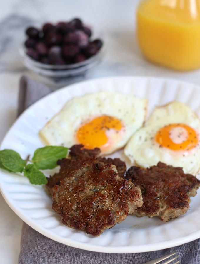 Three Homemade Breakfast Sausages on a white plate with sunny side up eggs.