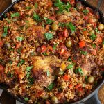 Chicken and Chorizo with rice, green olives, red bell pepper and garnished with parsley.