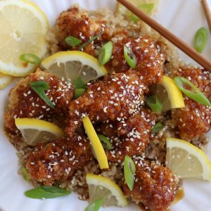 Chinese Lemon Chicken that has been baked and garnished with sesame seeds, lemon slices and green onions.