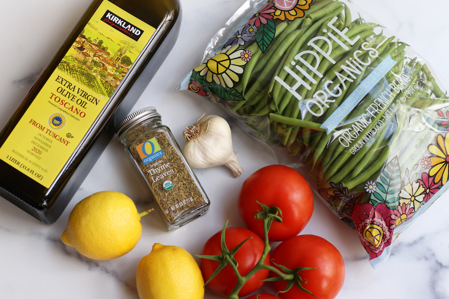 Ingredients for Green Bean and Tomato Salad lay on a white marble countertop.