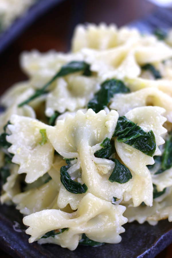 Creamy Bow Tie Pasta with spinach on a wavy grey plate.