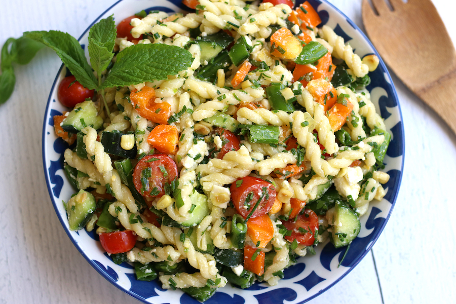 Healthy Pasta Salad for summertime sitting next to a wooden spoon and on a white wooden table.