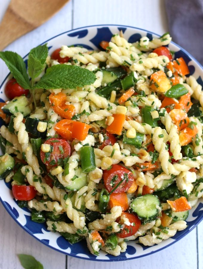 Overhead photo of Summer Pasta Salad with orange bell pepper pieces, fresh mint and chives.