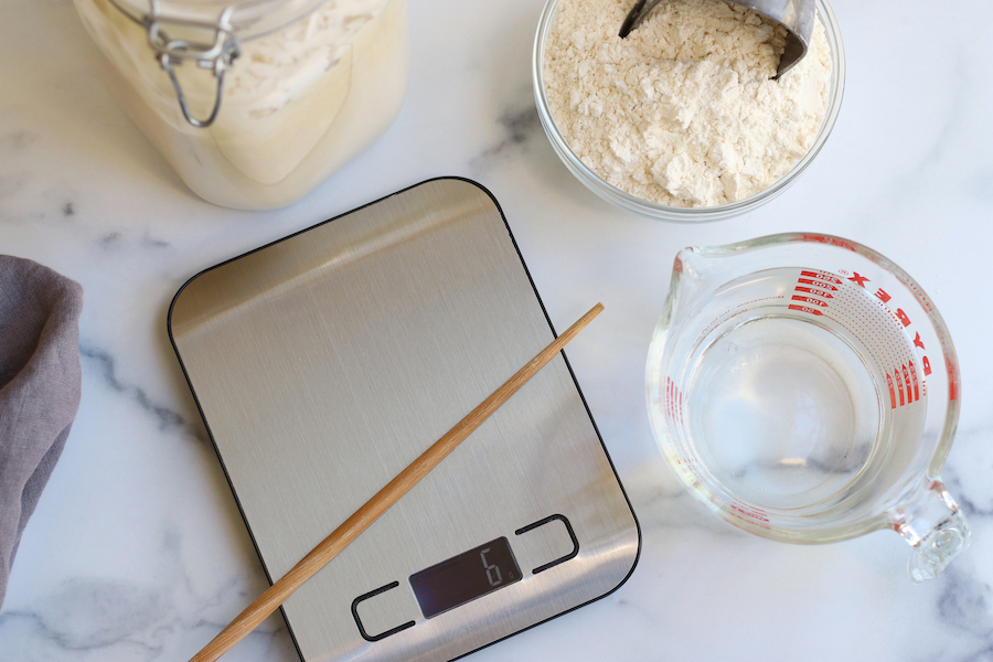 Most of the tools and ingredients needed for Homemade Sourdough Baguettes sitting on a white countertop.