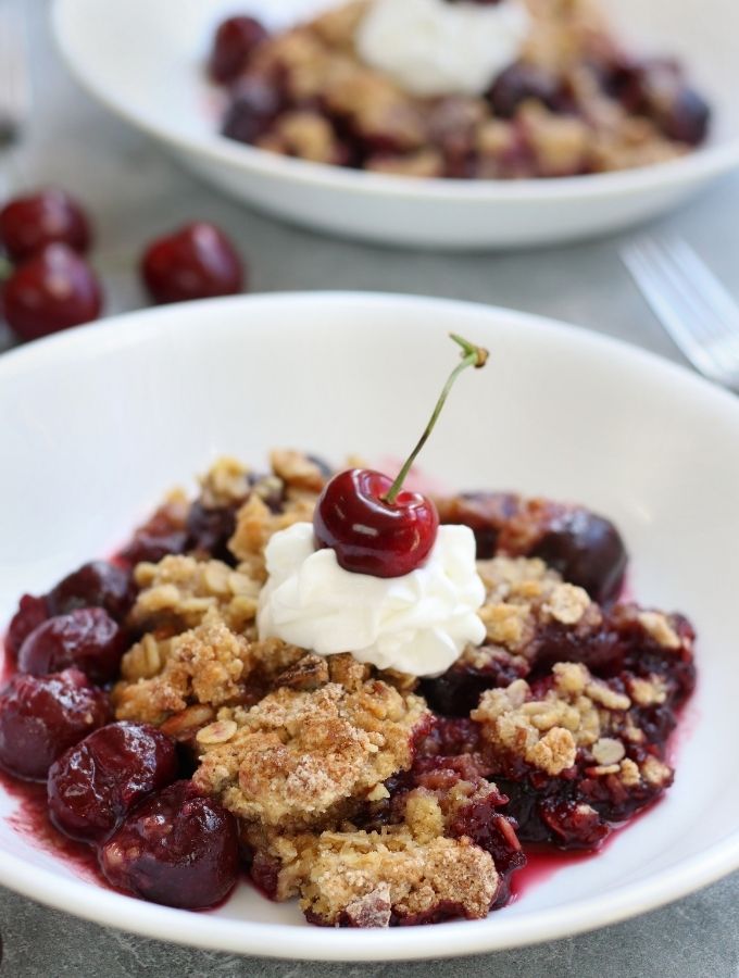 Cherry Crisp topped with a dollop of whipped cream and a fresh cherry.