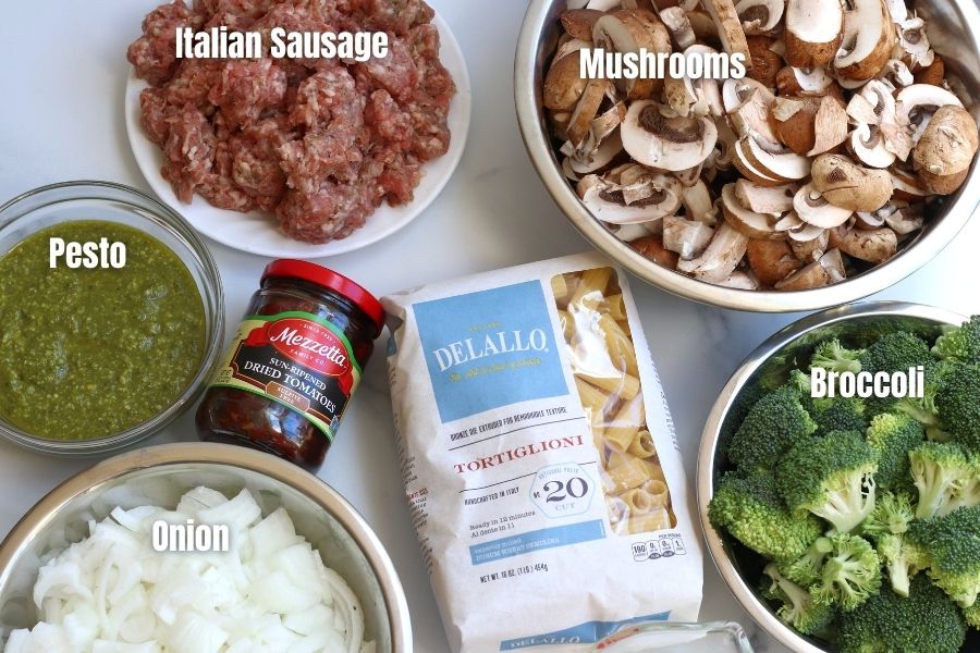 Ingredients for Sausage Pesto Pasta laid out on a white countertop.