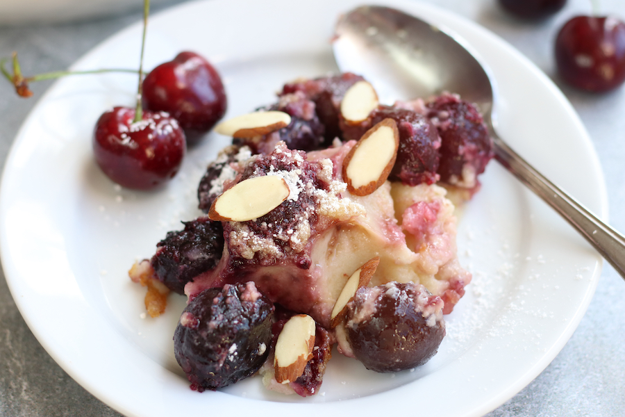 A serving of Cherry Clafouti on a white plate garnished with sliced almonds.