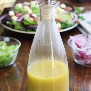 Apple Cider Vinaigrette in a glass salad dressing bottle sitting on a wooden table.