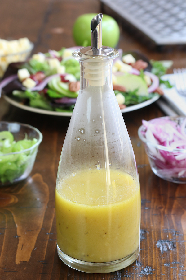 Apple Cider Vinaigrette in a glass salad dressing bottle sitting on a wooden table.