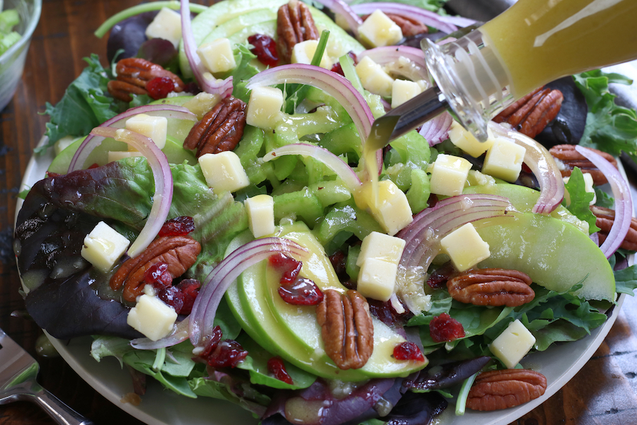 Apple Cider Vinegar Salad Dressing being poured on a green salad with fruit.