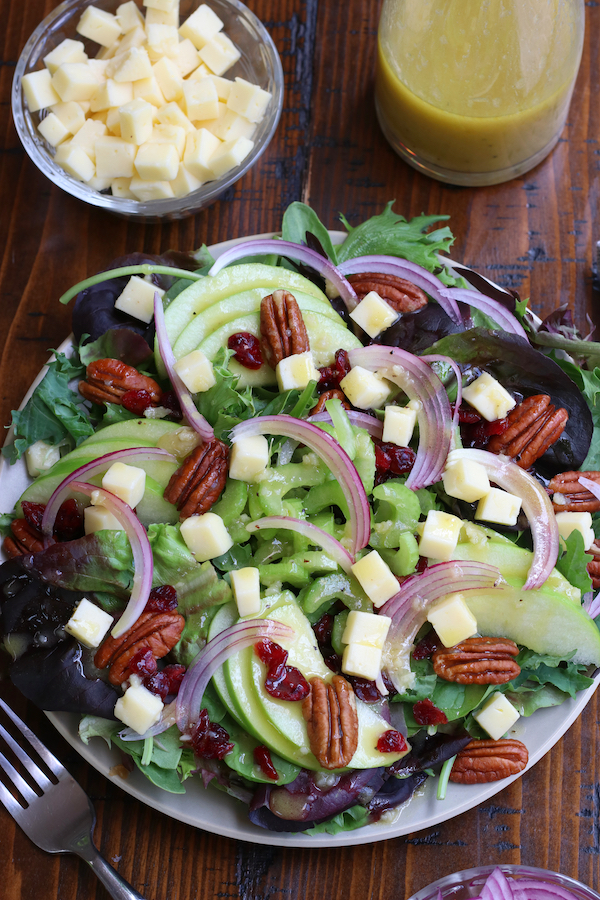 A plate of salad with apple and pecans sitting on a brown wooden table.