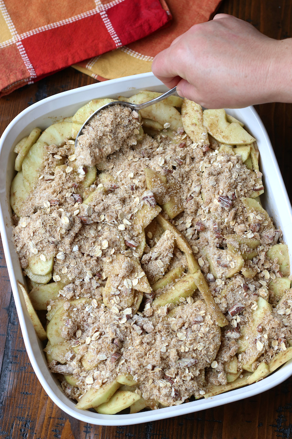 Adding crumble mix topping to apple pie filling fo Apple Crisp Recipe.