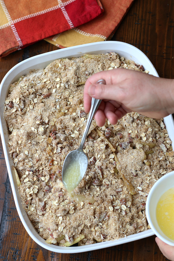 Adding melted butter to the top of Apple Crisp Recipe with oats.