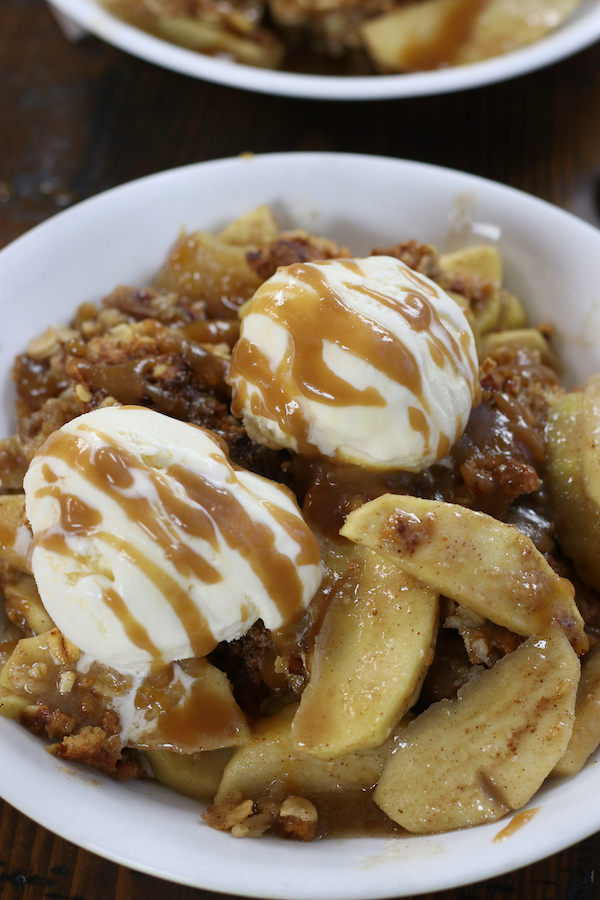 Apple Crisp with Oats served in a bowl with ice cream and caramel sauce.
