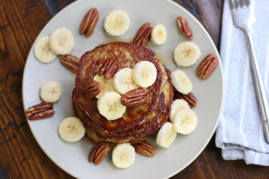 Overhead photo of Banana Oat Pancakes garnished with slices of banana and pecan halves.