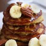 A stack of Oat Banana Pancakes with cut banana slices and pecans.