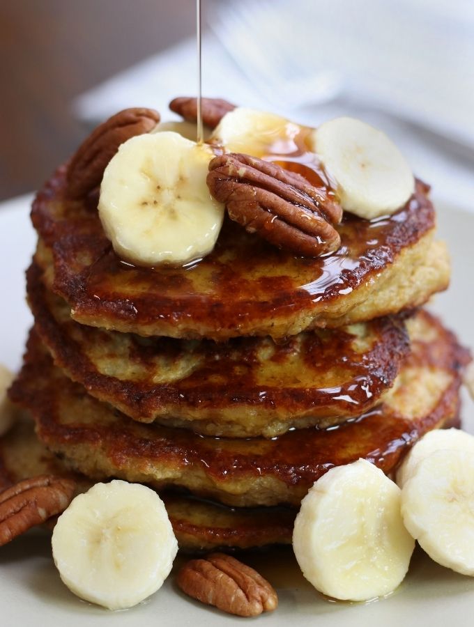 A stack of Oat Banana Pancakes with cut banana slices and pecans.