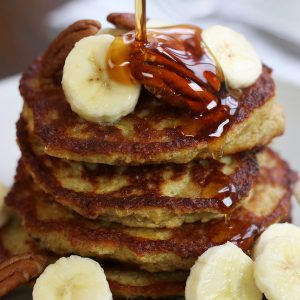 Maple syrup being poured on a stack of Oatmeal Banana Pancakes.