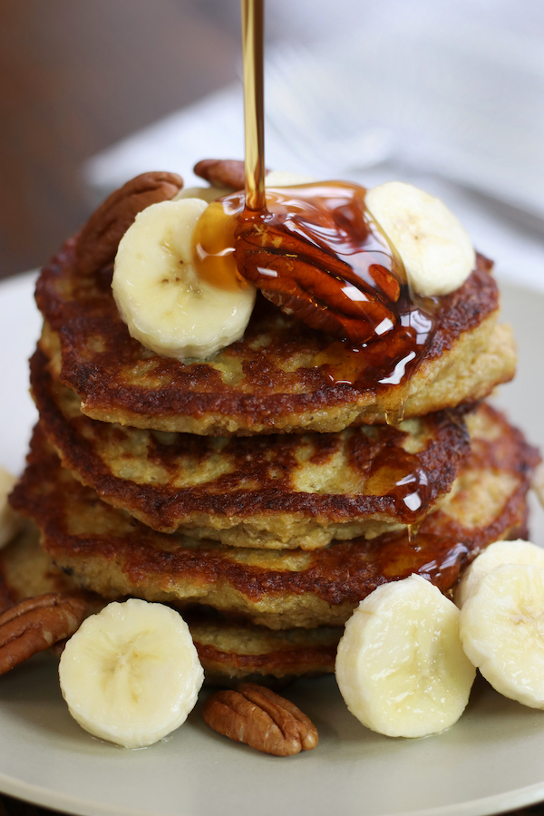 Maple syrup being poured on a stack of Oatmeal Banana Pancakes.