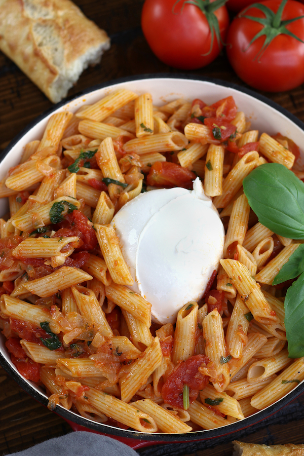 Overhead photo of Cheesy Penne Pasta sitting next to fresh tomatoes and a piece of baguette bread.