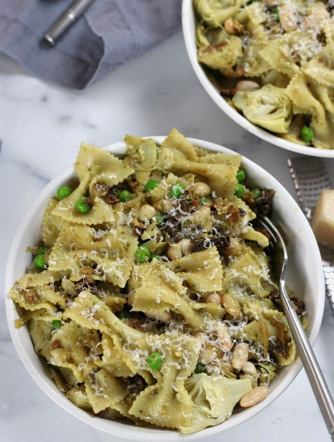 Pasta with White Beans in a white bowl with shaved parmesan on top.