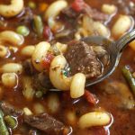 A spoonful of Beef Noodle Soup with a curly noodle and tender beef.