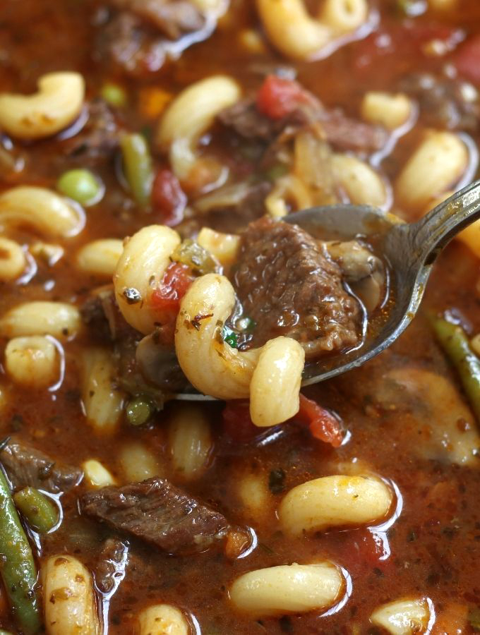 A spoonful of Beef Noodle Soup with a curly noodle and tender beef.