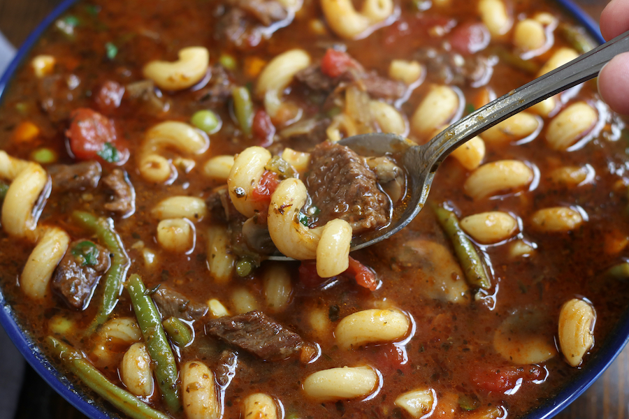 A spoonful of Vegetable Beef Noodle Soup being eaten form a blue bowl.