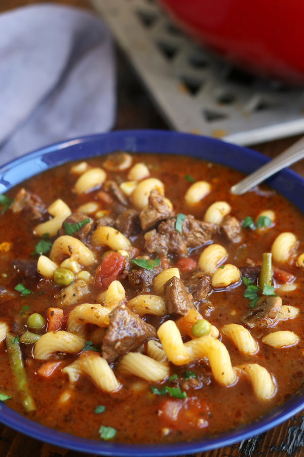 A big bowl of Vegetable Beef Soup with tomatoes, peas, green beans and mushrooms.