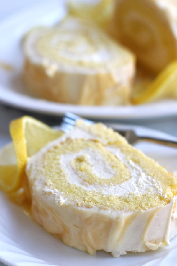 A slice of Lemon Curd Swiss Roll on a small white plate with a lemon slice.