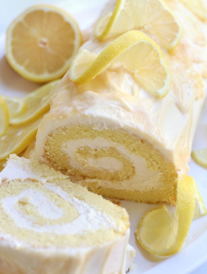 Lemon Roll Cake on a white platter surrounded by lemon slices.
