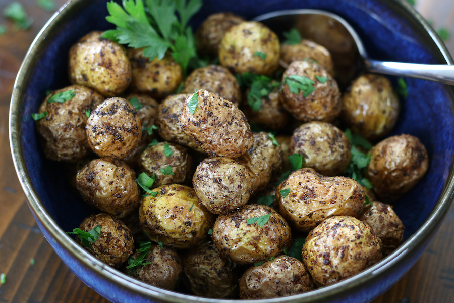 Well seasoned Air Fryer Tiny Potatoes served in a bowl that is sitting on a wooden table.
