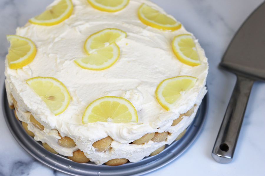 A round cake made from Limoncello Tiramisu Recipe sitting next to a pie server.